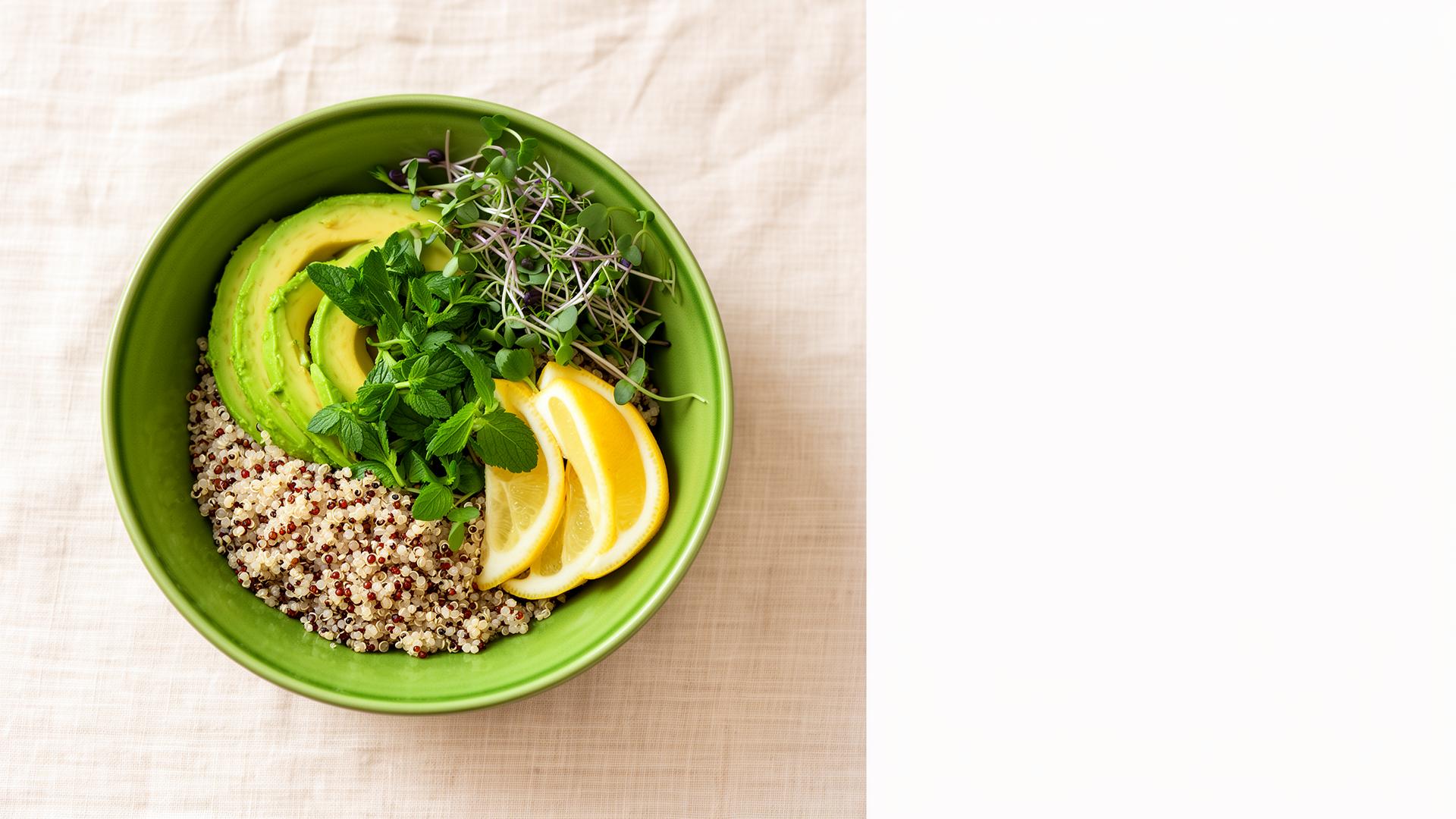 A green ceramic bowl filled with quinoa, avocado and herbs